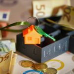 Llavero de casa naranja, monedas y dinero sobre la mesa.