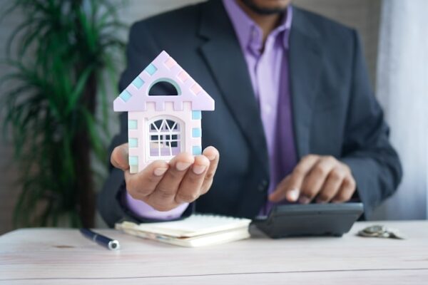 Hombre con traje sosteniendo una casa y en la otra mano una calculadora.